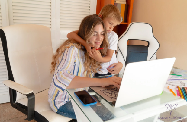 Mother working on laptop at home with child beside her